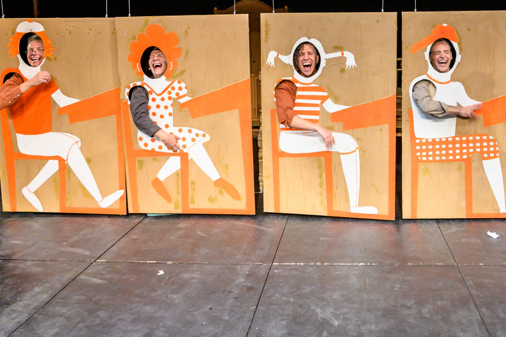 Vier Personen hinter bunten Holzpaneelen mit lustigen Kostümen und fröhlichen Gesichtsausdrücken.