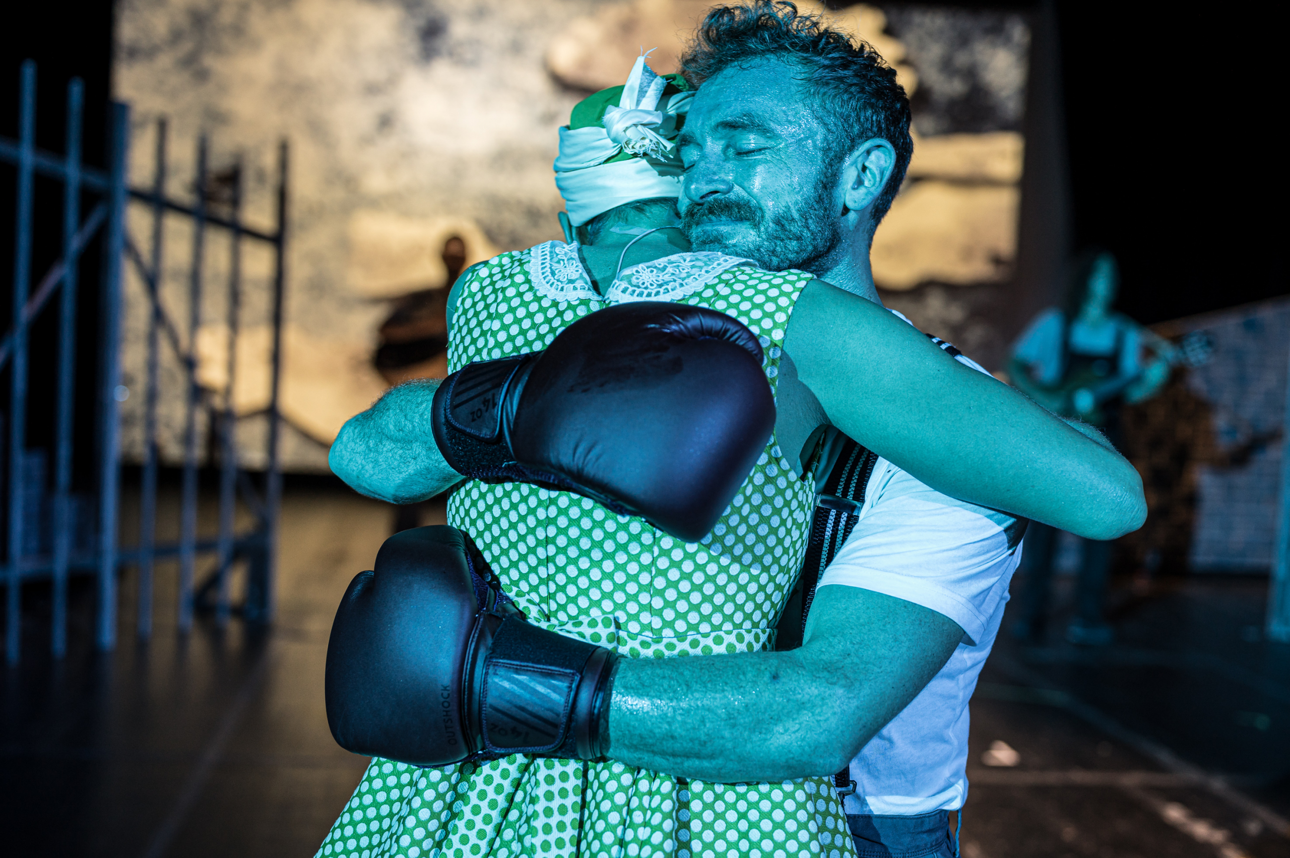 Umarmung zwischen einem Boxer in Handschuhen und einer Frau im gelben Kleid auf der Bühne.