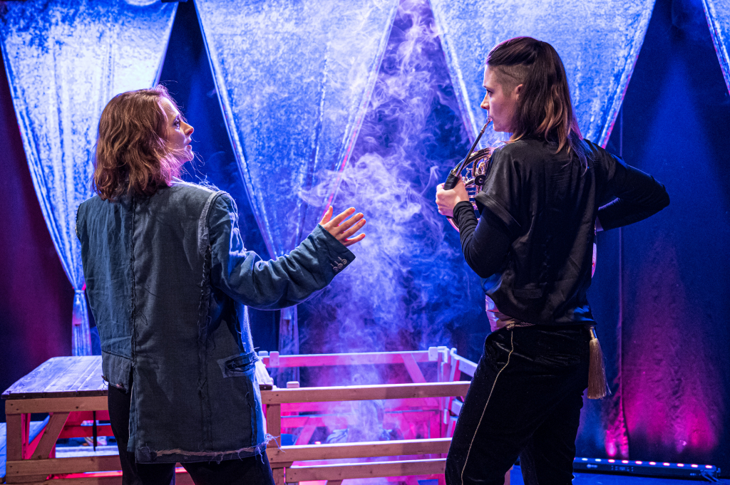 Szene aus dem Theaterstück mit zwei Schauspielerinnen, die im Nebel während einer Aufführung stehen. EIne der Schauspielerinnen spielt ein Horn.