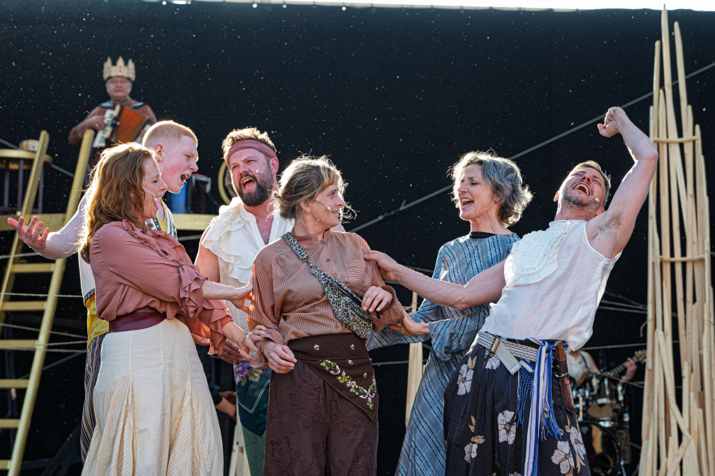 Theateraufführung mit Schauspielern in historischen Kostümen auf der Bühne, die jubeln und sich freuen.