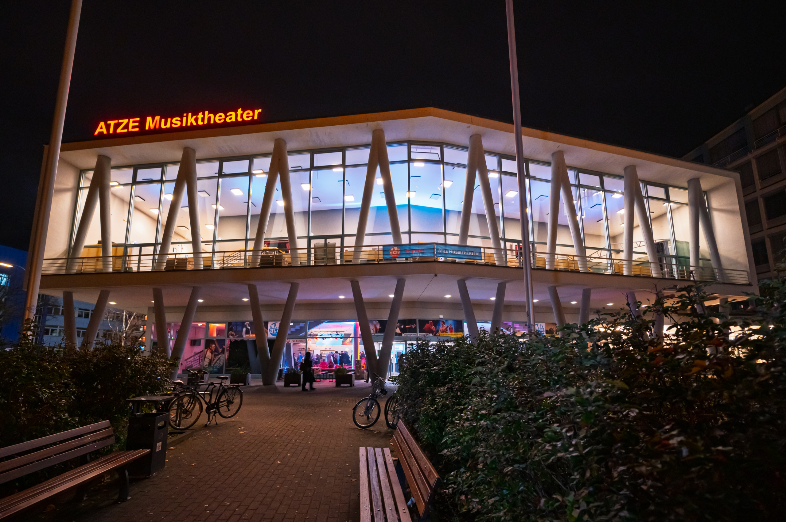Das moderne Gebäude des ATZE Musiktheaters mit großen Glasfronten und beleuchtetem Schriftzug bei Nacht
