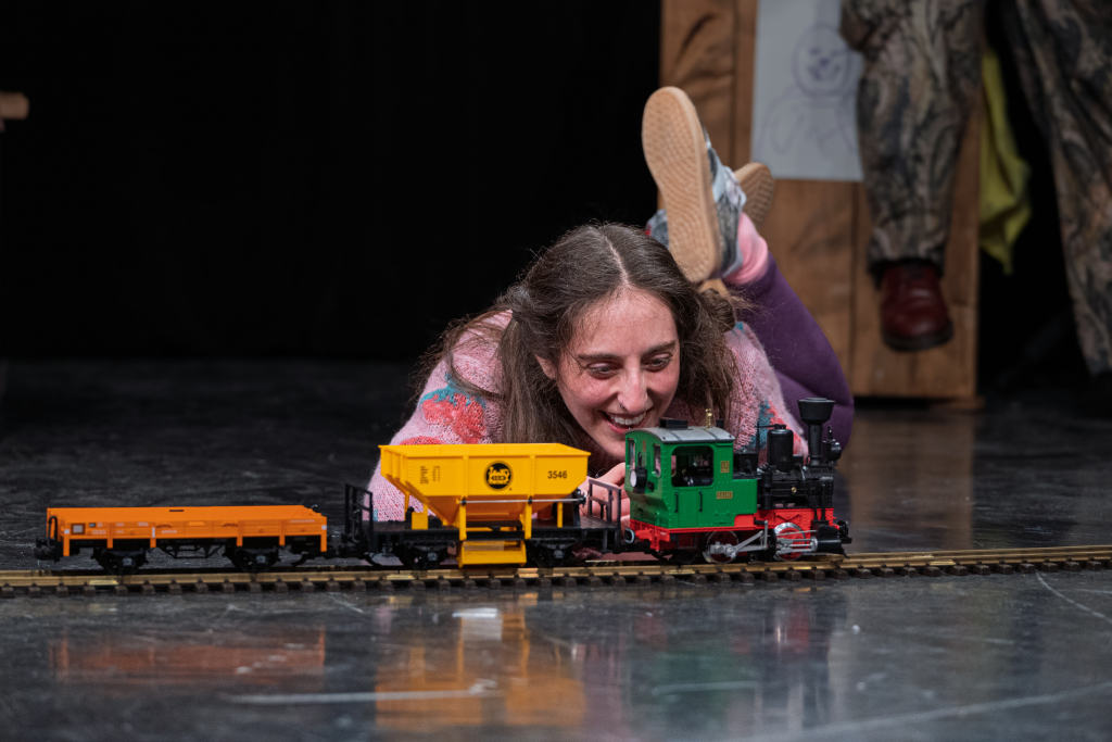 Eine junge Frau liegt auf dem Boden und schaut einer elektrischen Eisenbahn beim fahren zu.