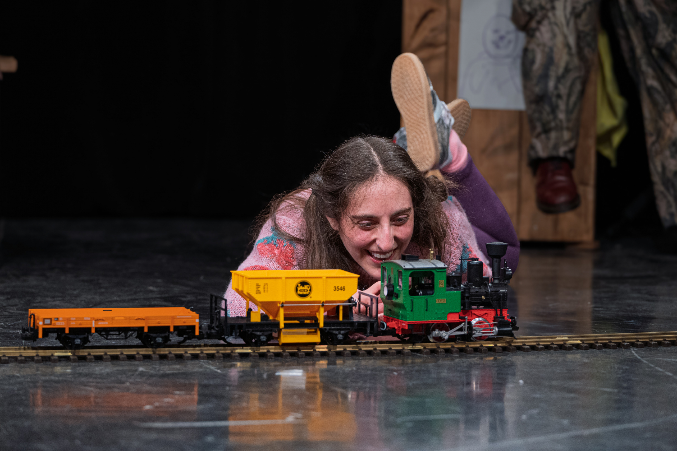 Eine junge Frau liegt auf dem Boden und schaut einer elektrischen Eisenbahn beim fahren zu.