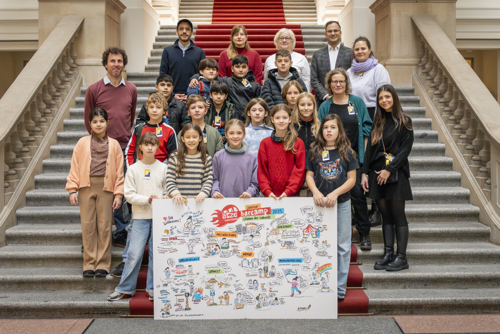 Gruppe von Menschen steht auf einer Treppe hinter einem großen, bunten Plakat mit Zeichnungen und Texten.