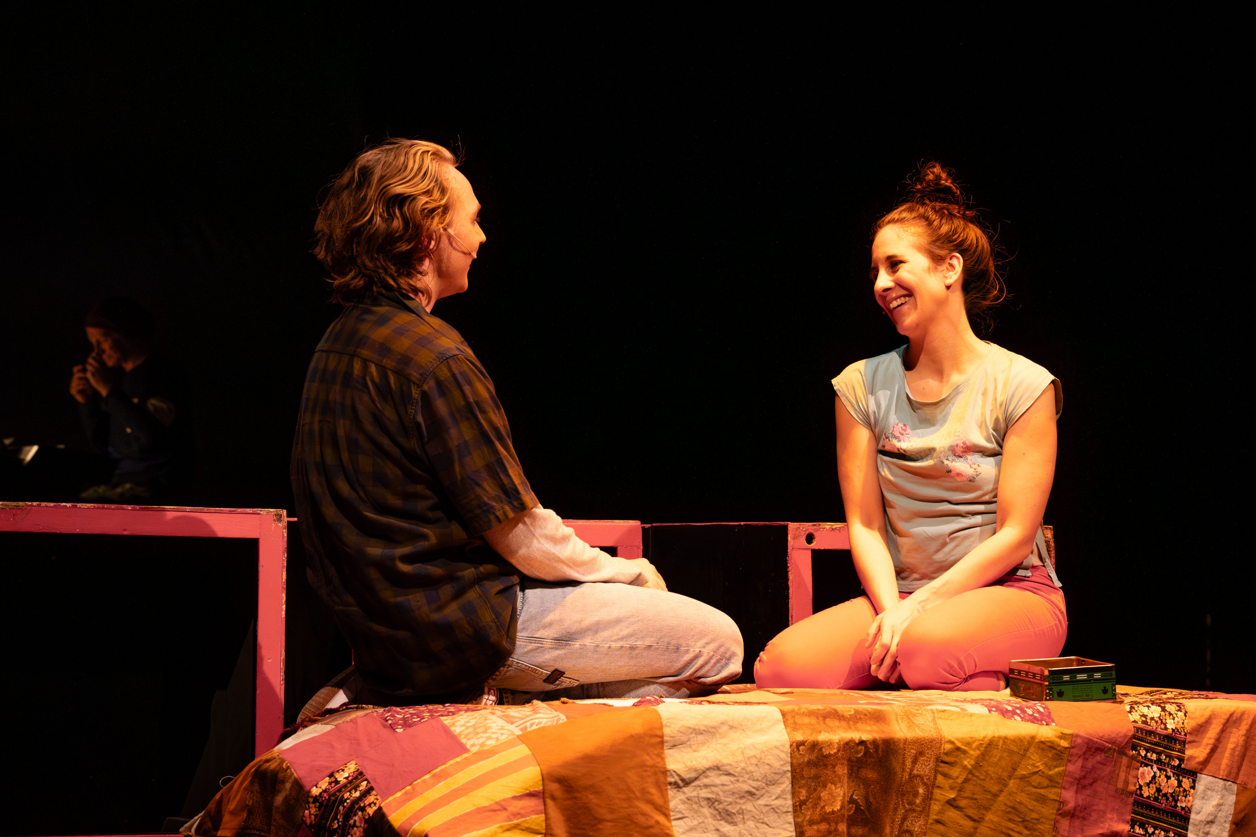 Zwei Personen sitzen sich auf einem bunt gemusterten Bett gegenüber.