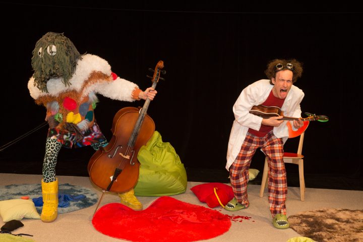 Zwei Personen mit bunter Kleidung: einer spielt Cello, der andere singt.