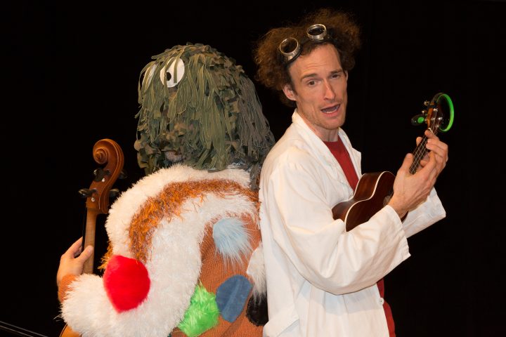 Zwei Personen stehen Rücken an Rücken: einer mit Ukulele und einer mit Geige.