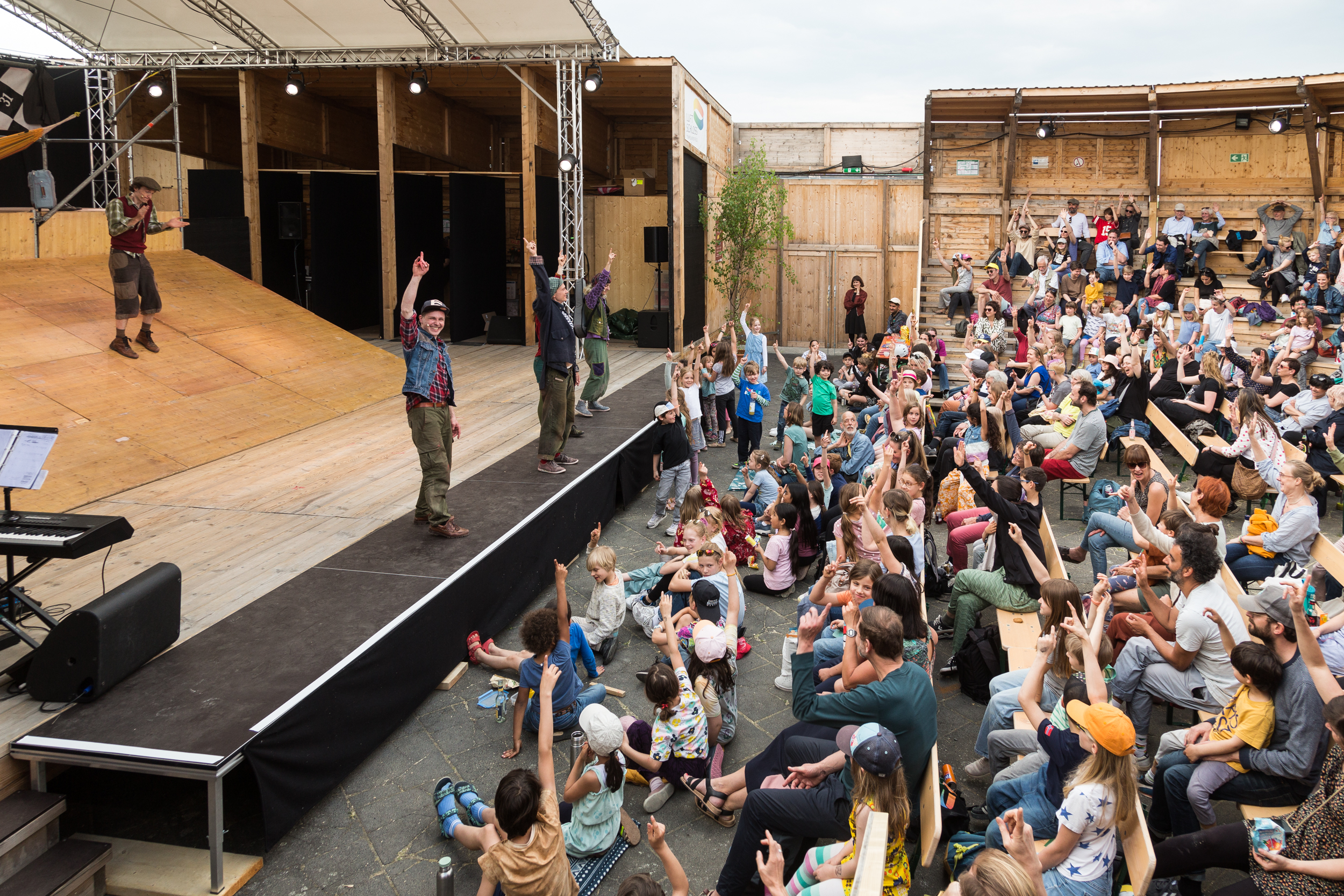 Mehrere Darsteller auf einer Bühne vor einem Publikum aus Kindern und Erwachsenen, die mit erhobenen Armen reagieren