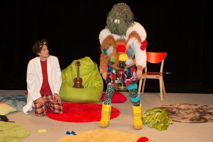 Zwei Personen mit buntem Kostüm einer kniend und der Andere stehend auf einem bunten Teppich