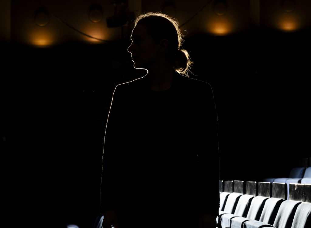 Silhouette einer Frau in einem Theater zwischen leeren blauen Sitzen im Hintergrund.