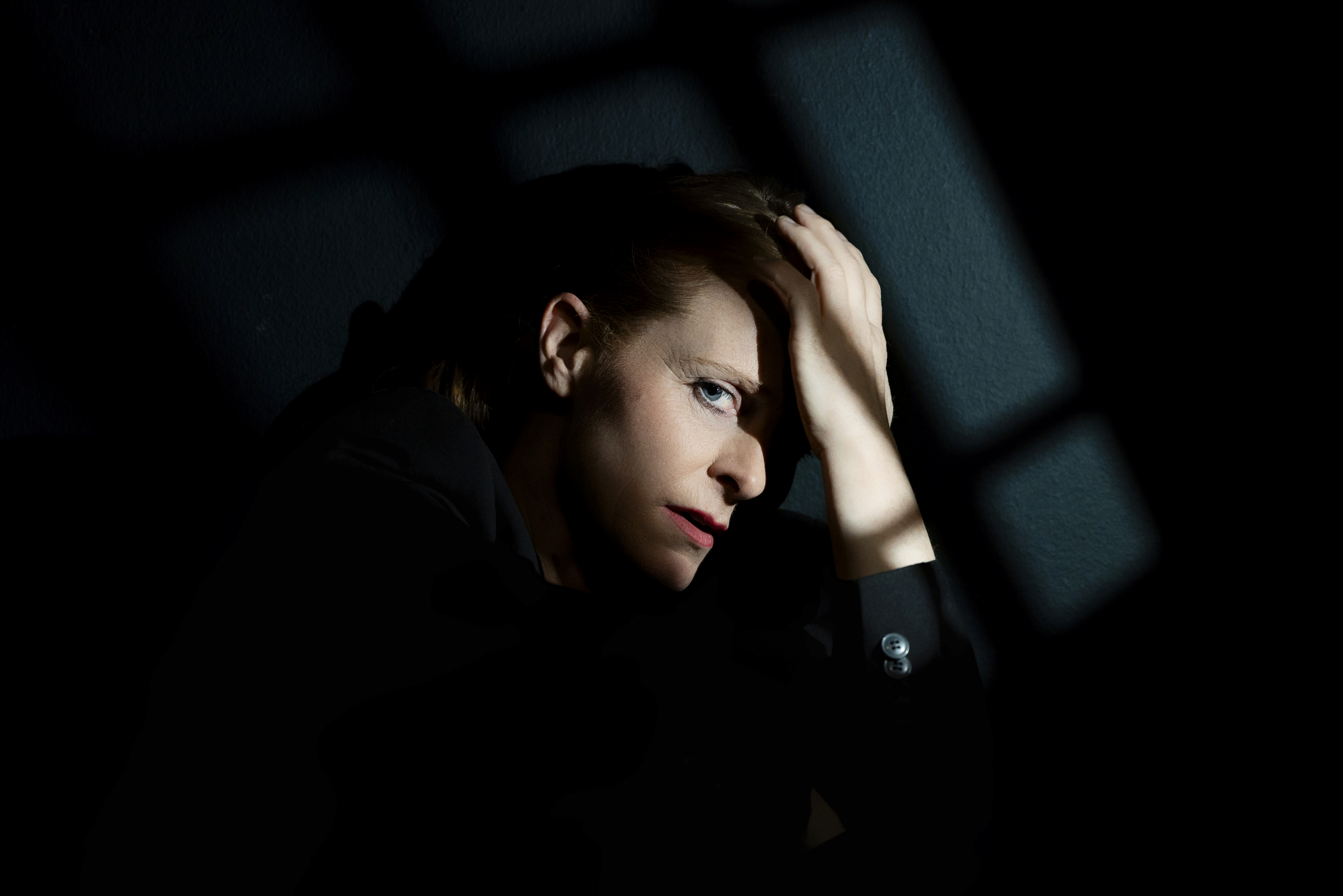 Frau mit gestrecktem Arm und Hand auf der Stirn, in dunklem Raum mit Lichtspielen.