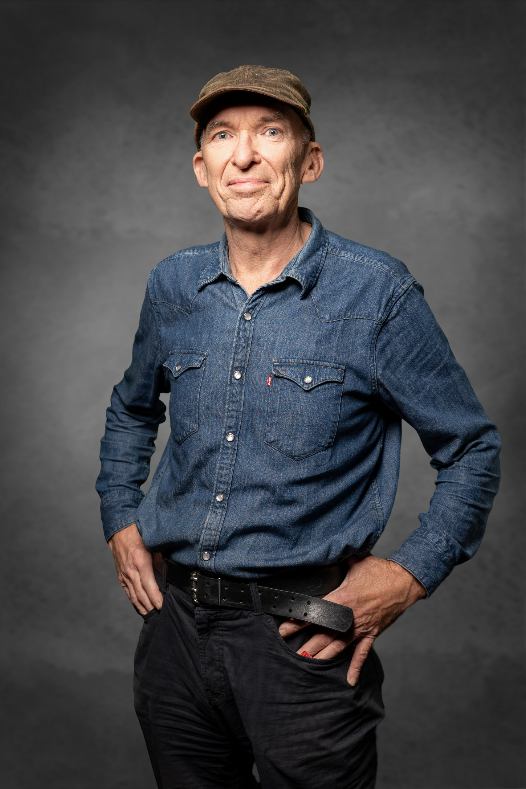 Ein Mann in einem blauen Jeanshemd und Basecap steht mit Händen in den Hüften da.