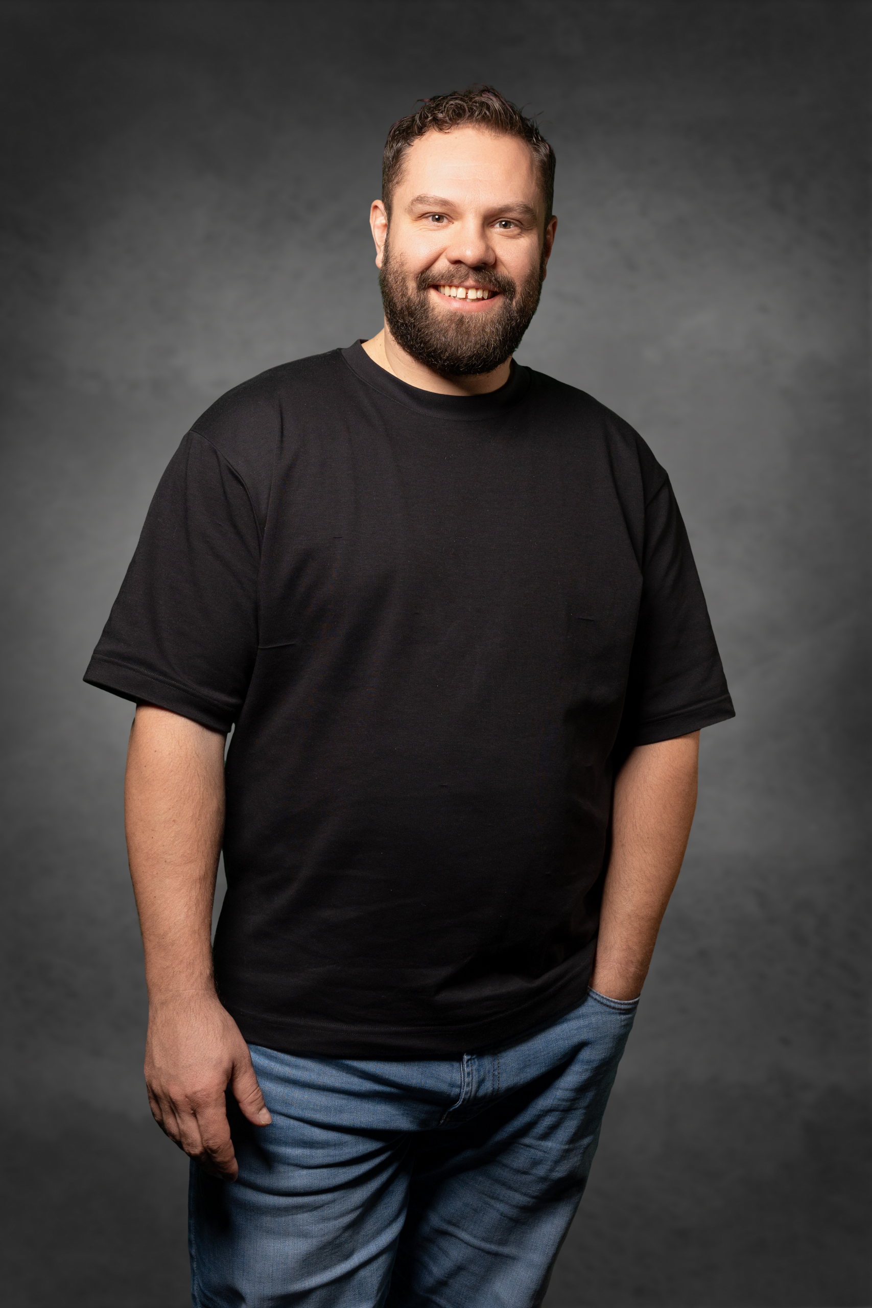 Mann mit Bart und schwarzem Shirt, lächelnd in lockerer Pose.