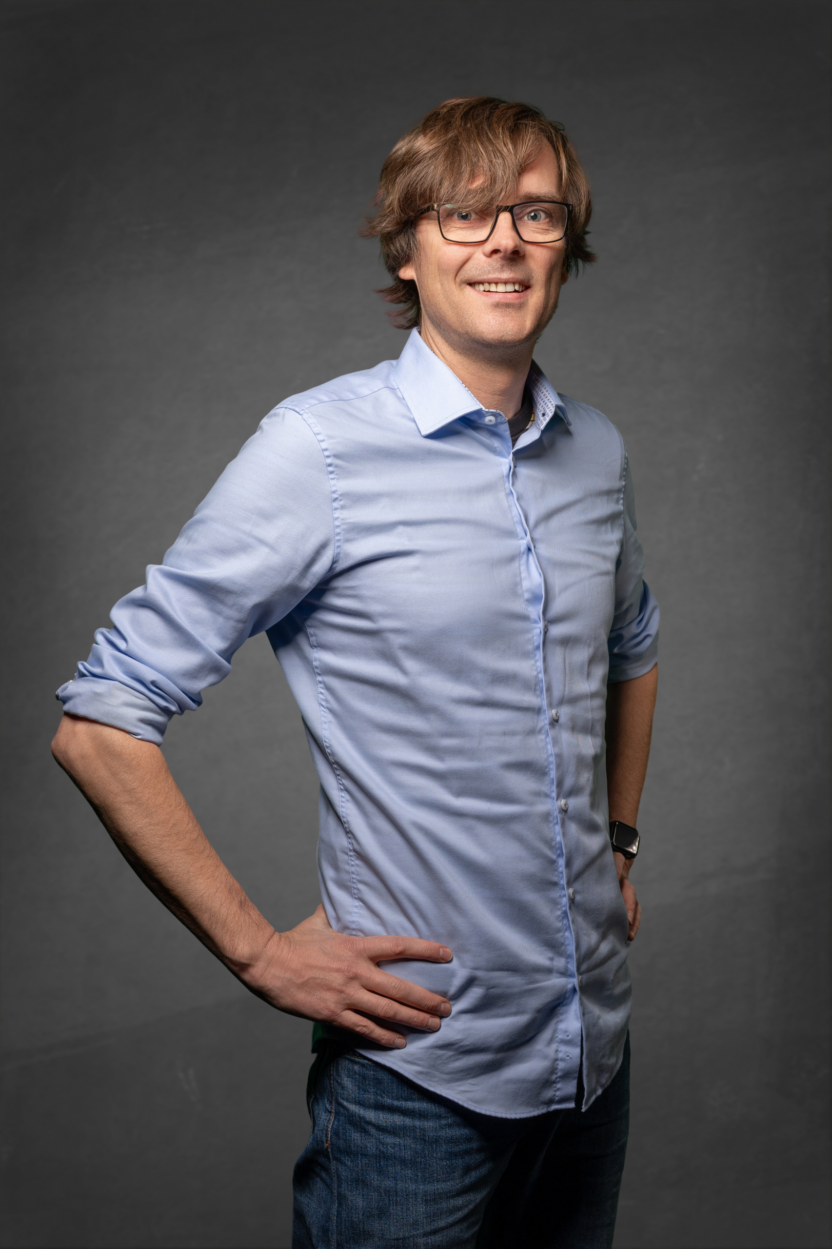 Modell in hellblauer Hemd und Jeans mit lässiger Pose vor neutralem Hintergrund.