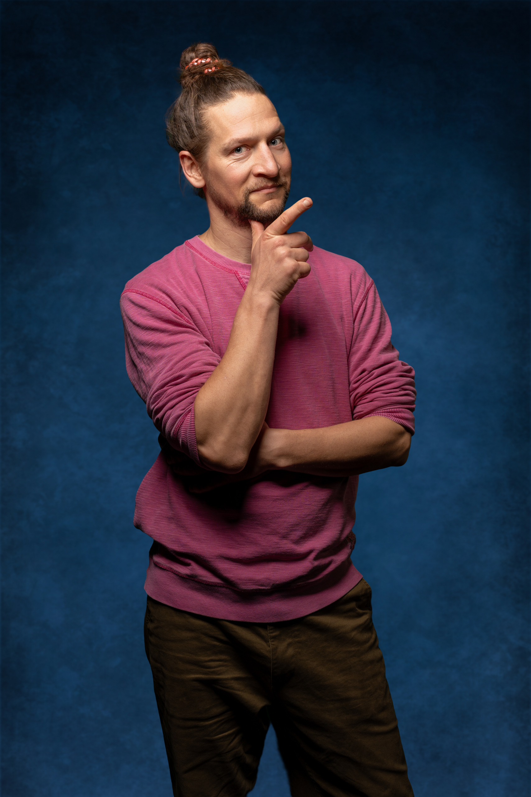 Portrait eines Mannes mit einem Denkpose in einem lila Sweatshirt vor einem blauen Hintergrund.