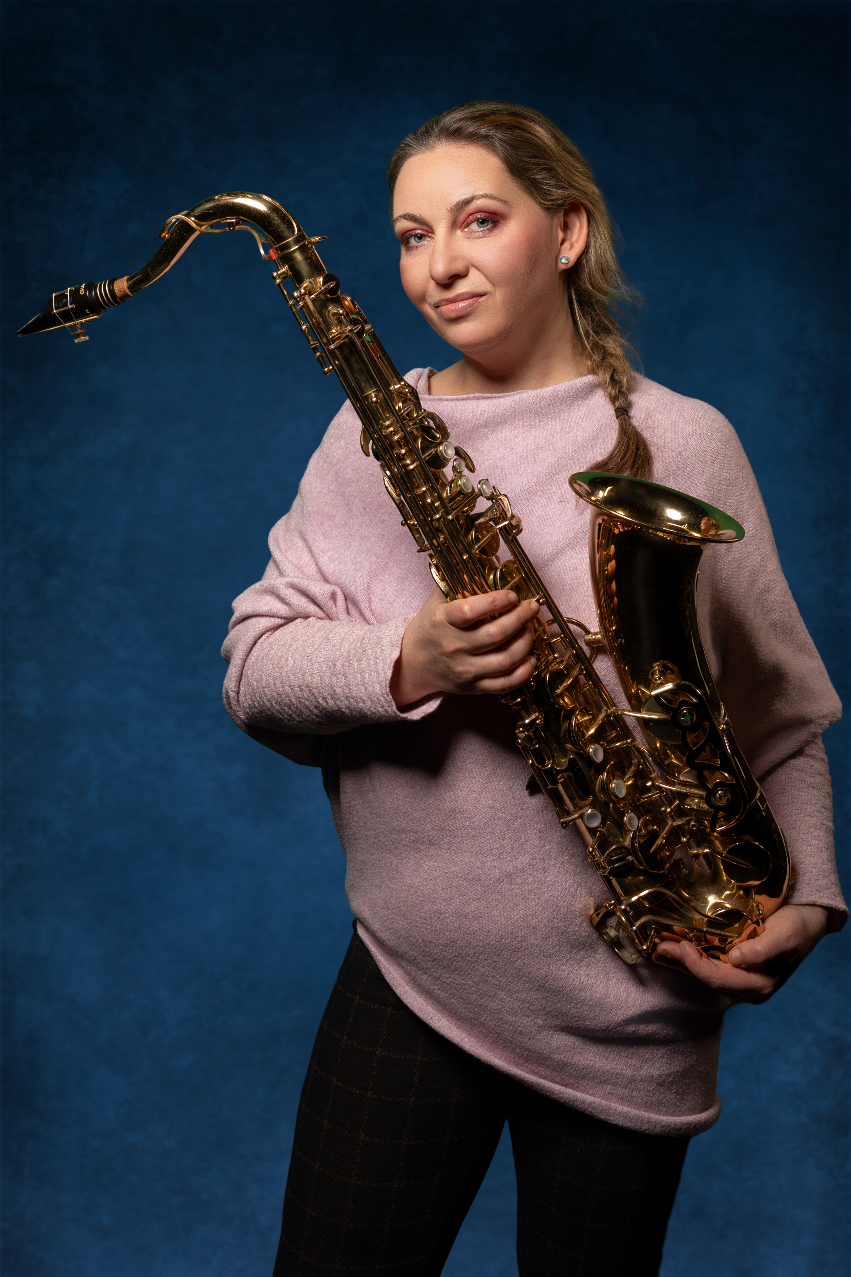 Frau mit Bluse hält ein goldenes Saxophon vor blauem Hintergrund.