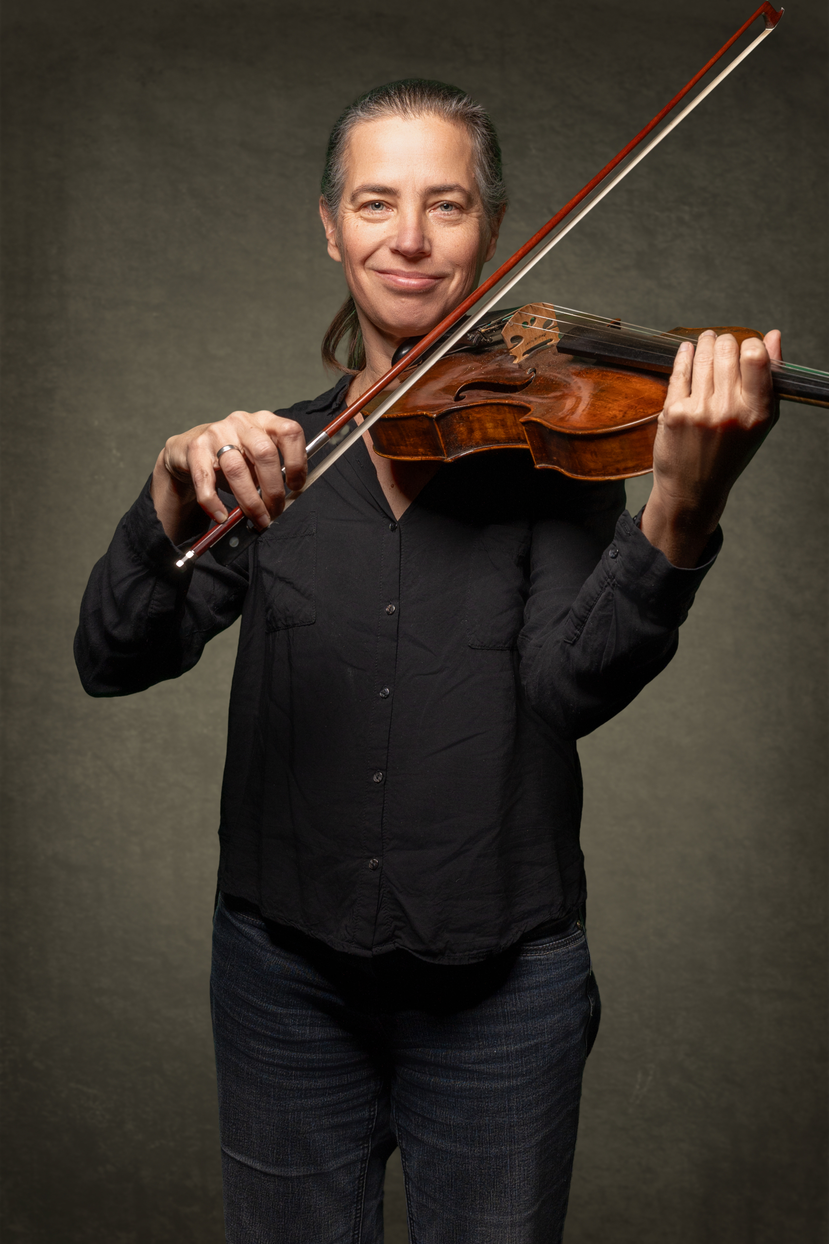 Dame spielt Geige mit braunem Korpus und Holzbogen, lächelt in eleganter Pose.