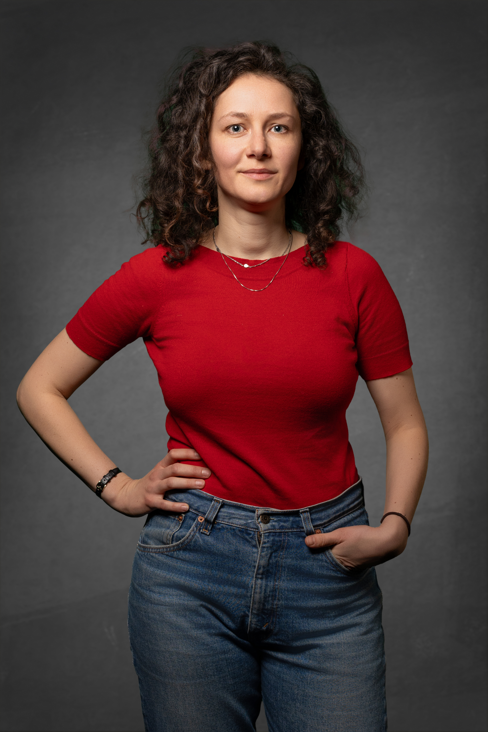 Frau in rotem T-Shirt und blauen Jeans, steht lässig mit der Hand in der Hosentasche.