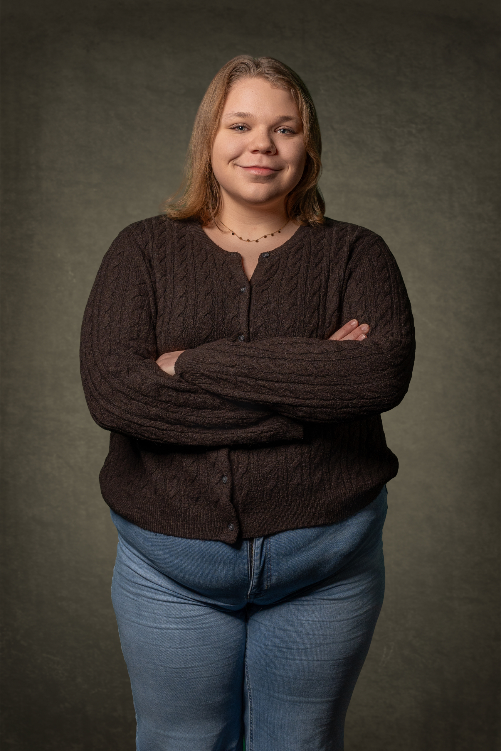 Schwarze Strickjacke mit Kabelmuster über blauem Jeans, Model mit verschränkten Armen und lächelndem Gesicht.