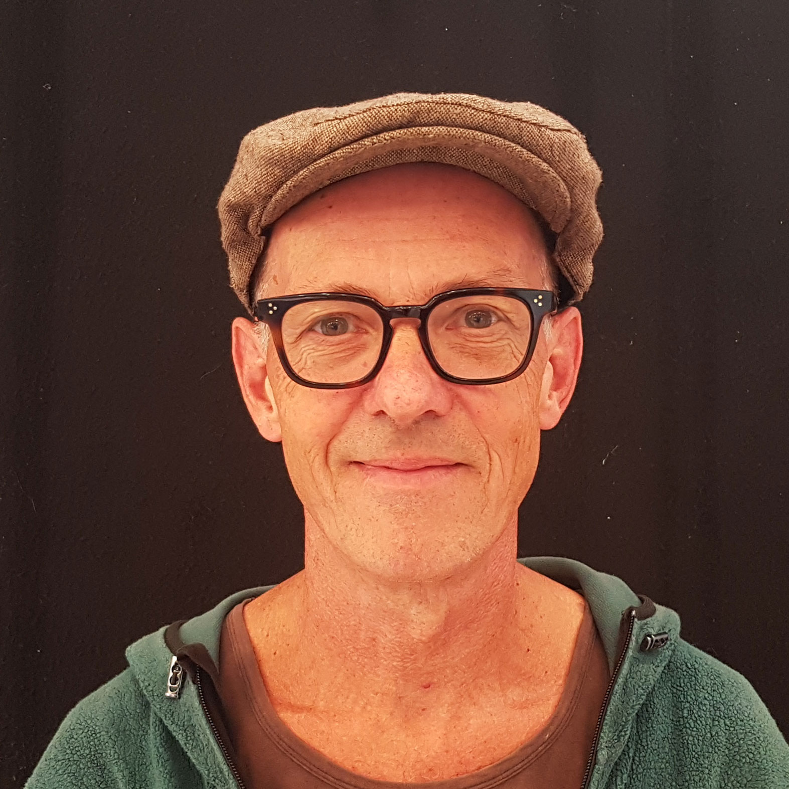 Porträt eines Mannes mit Brille, einer Schirmmütze und einem grünen Oberteil.