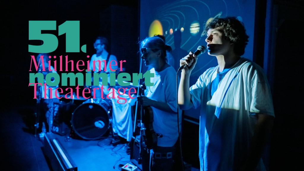 Drei Personen auf einer Bühne, eine hält ein Mikrofon, im Hintergrund Schlagzeug und Projektionen