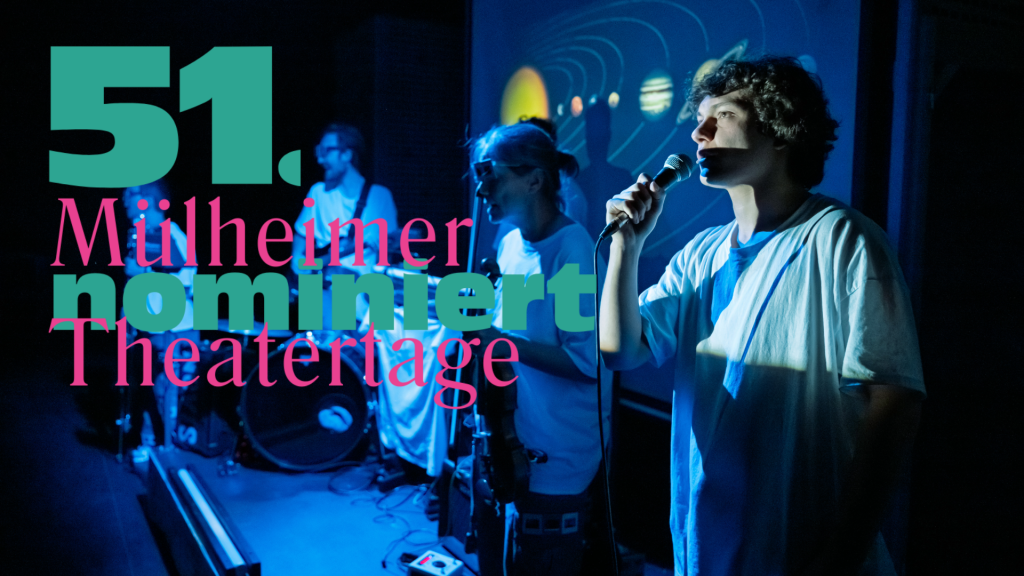 Drei Personen auf einer Bühne, eine hält ein Mikrofon, im Hintergrund Schlagzeug und Projektionen