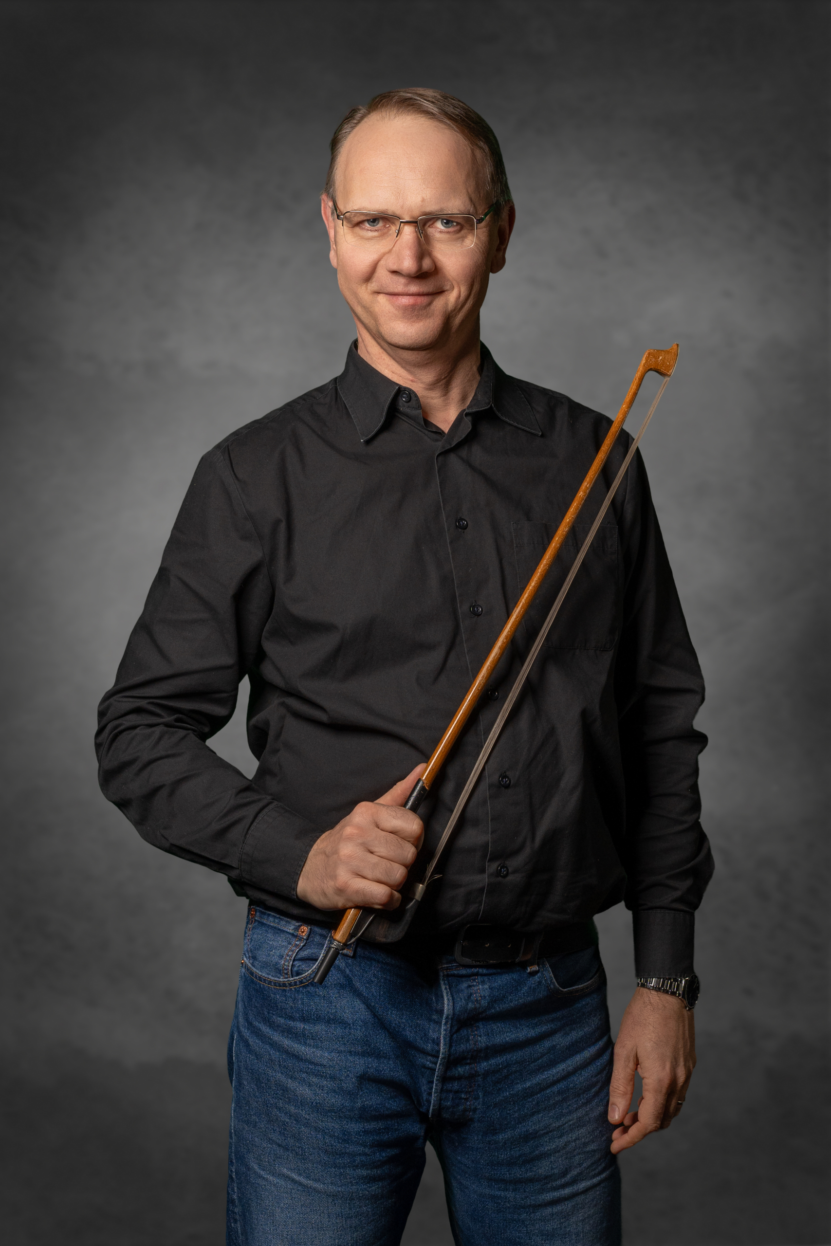 Porträt eines Mannes in schwarzem Hemd mit einem Geigenbogen in der Hand.