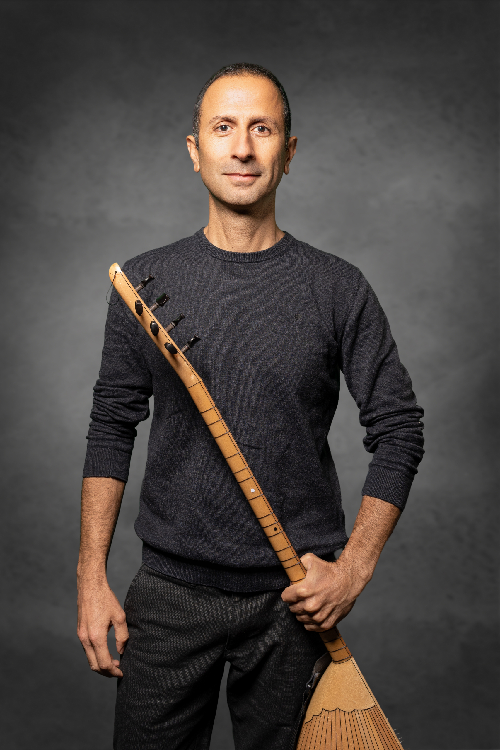 Mann in grauem Pullover steht mit einer traditionellen balalaika in der Hand.