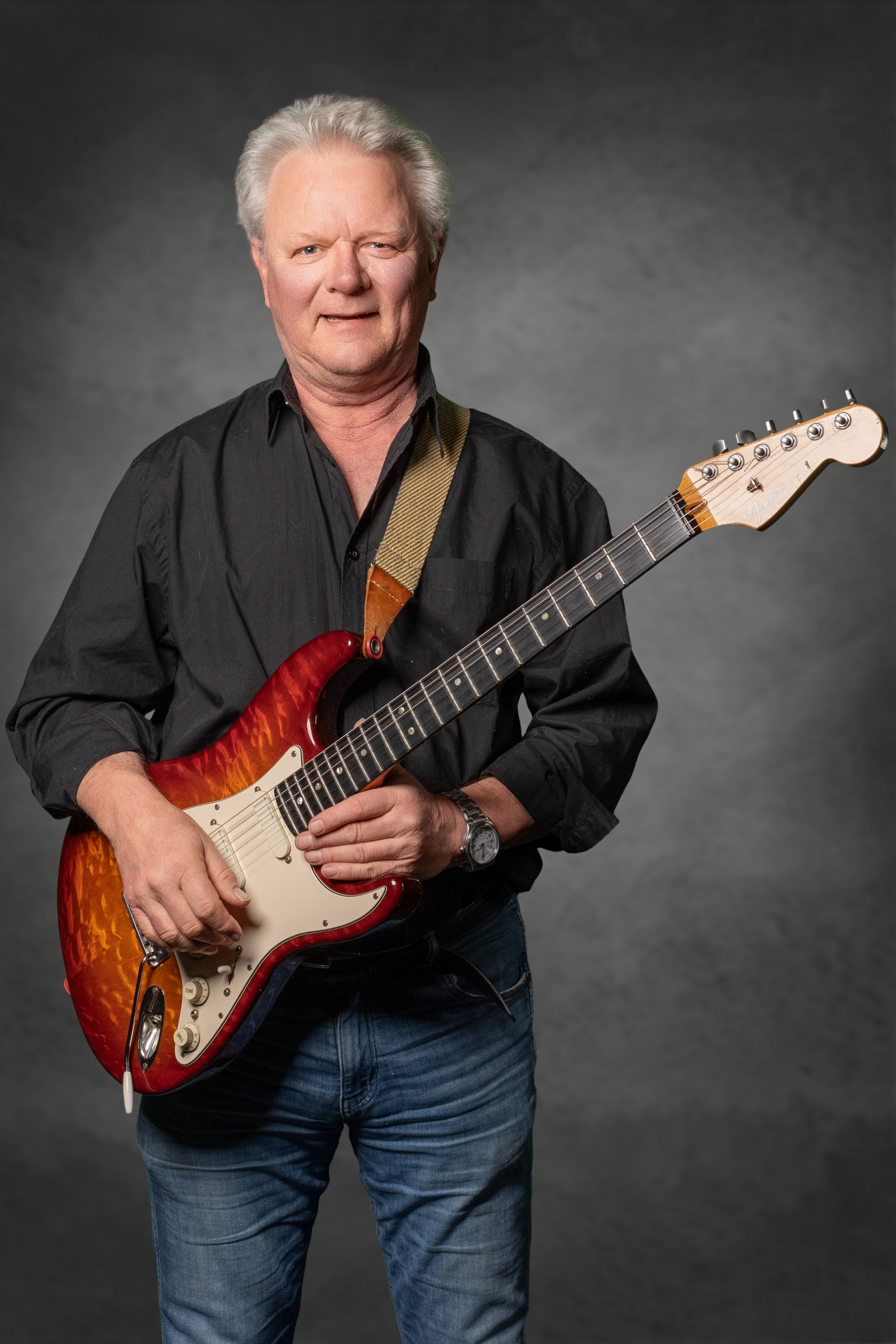 Mann mit Gitarre: Portrait eines musikbegeisterten Künstlers in schwarzem Hemd und blauen Jeans.