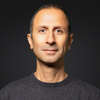 Mann mit kurzem Haar und dunklem Pullover vor schwarzem Hintergrund, frontal aufgenommen.