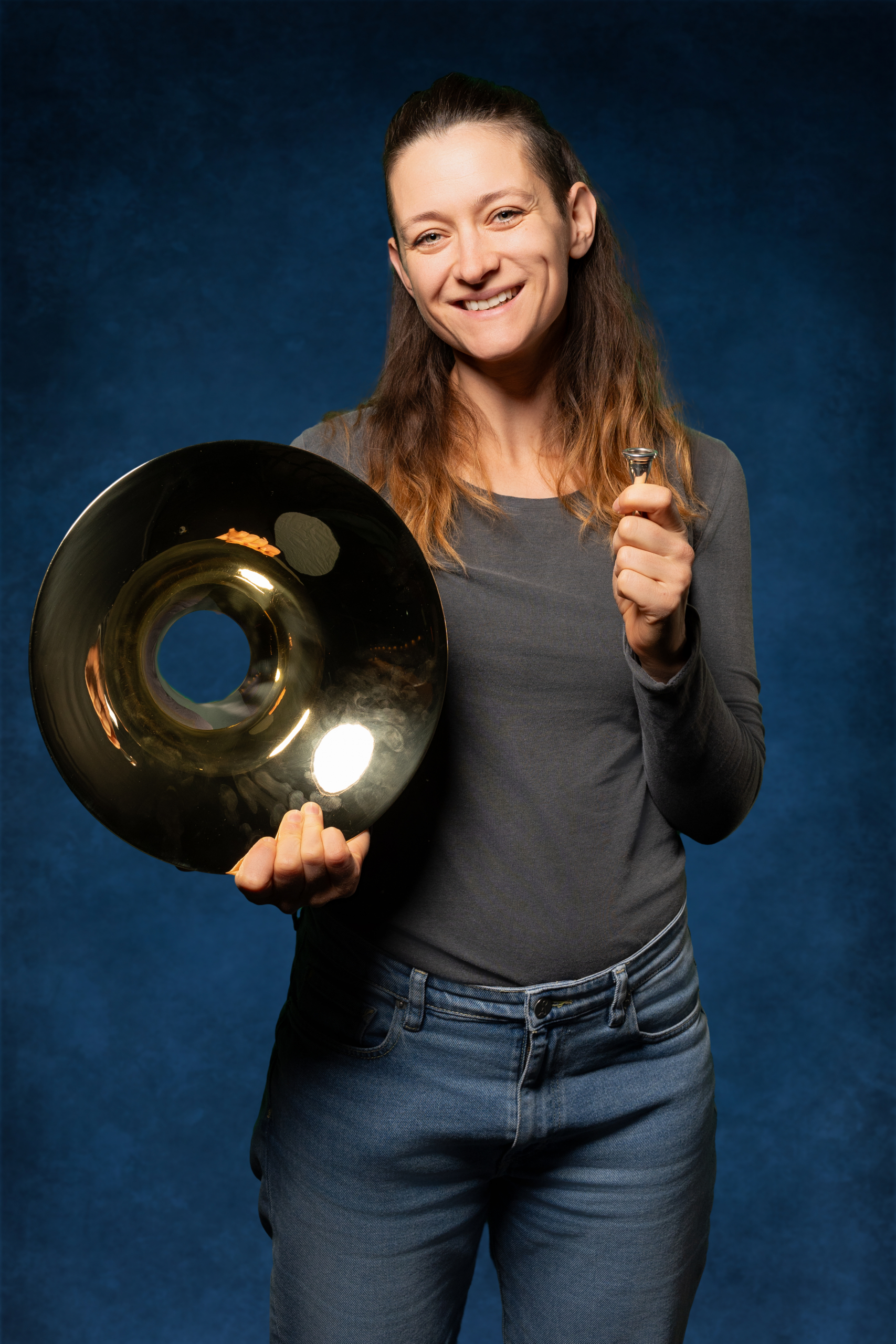 Lächelnde Frau hält eine goldene Trommel und ein Mundstück mit blauem Hintergrund.