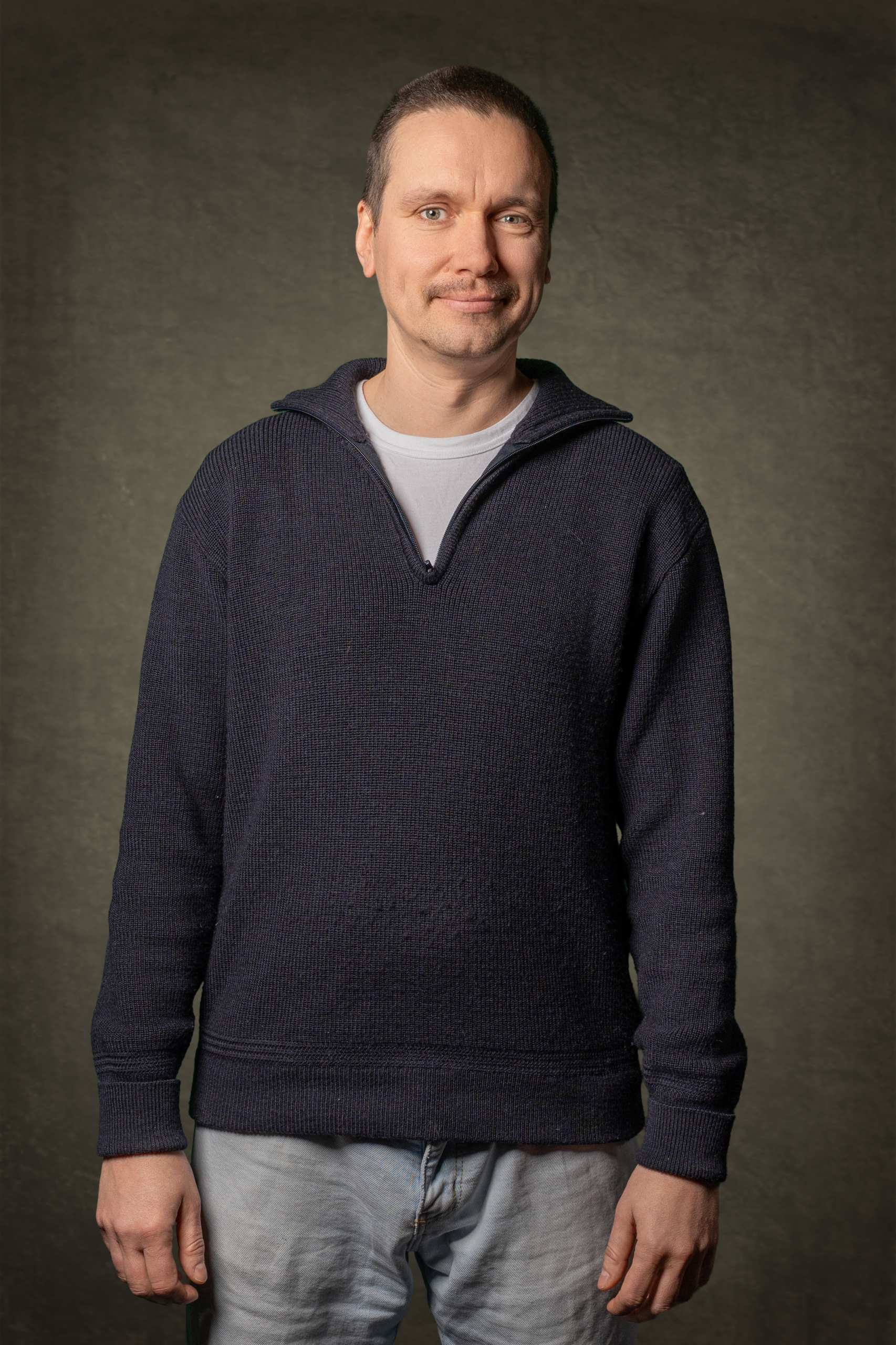 Mann im dunkelblauen Pullover mit Reißverschluss, auf neutralem Hintergrund portraitiert.
