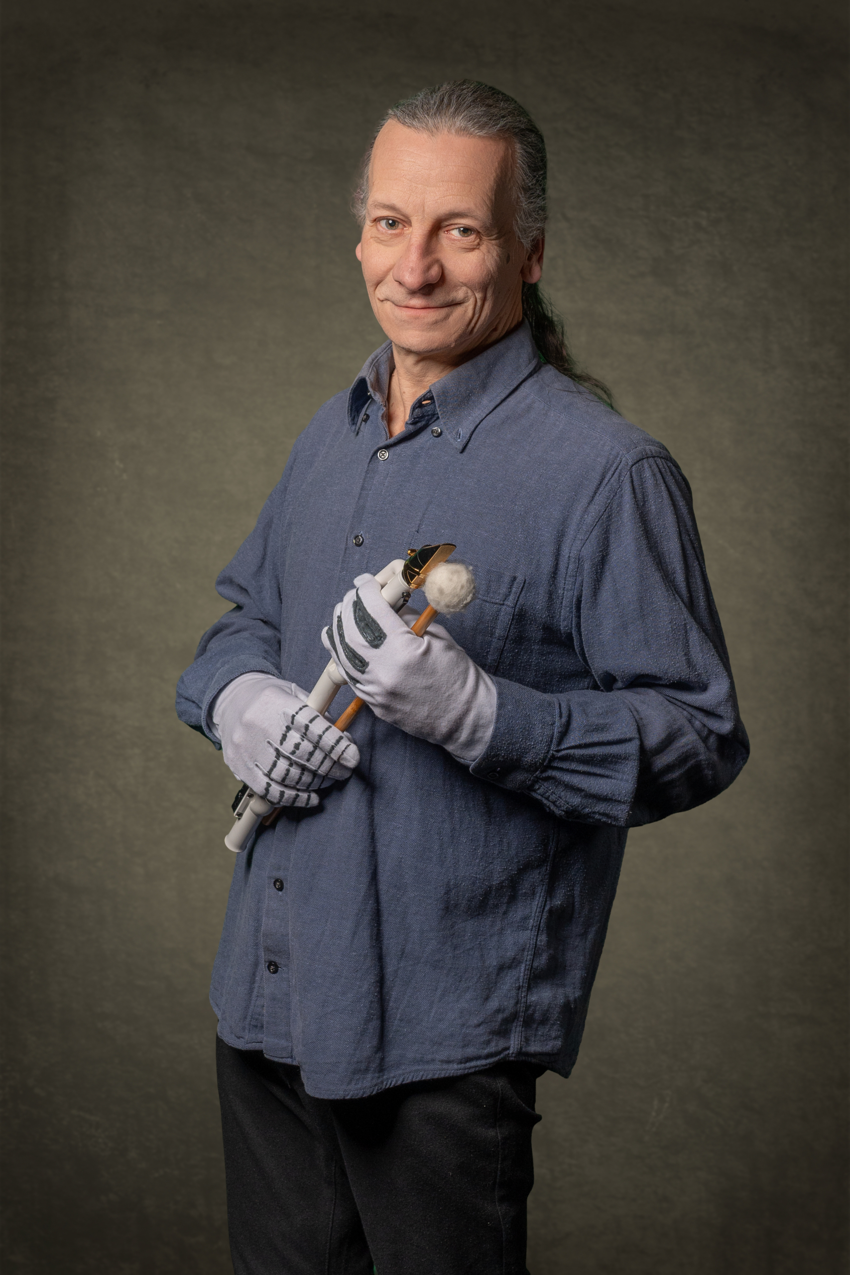 Mann mit Langarmhemd, hält Drumsticks in Handschuhen.