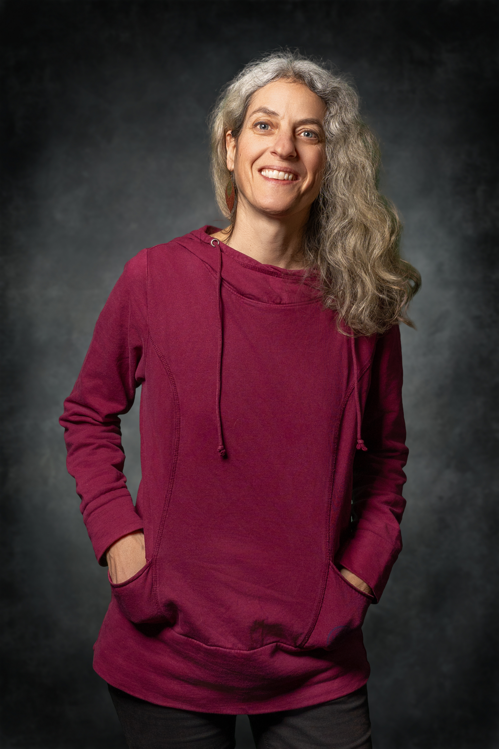 Frau mit grauen Haaren trägt einen weinroten Pullover mit Kapuze und Seitentaschen.