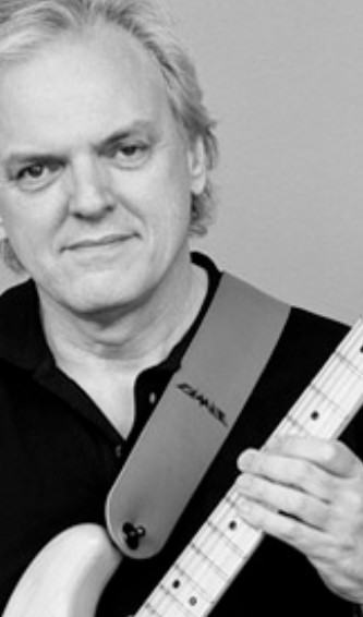 Porträt eines Mannes mit Gitarre, lächelnd und in Schwarz-Weiß Aufnahme.