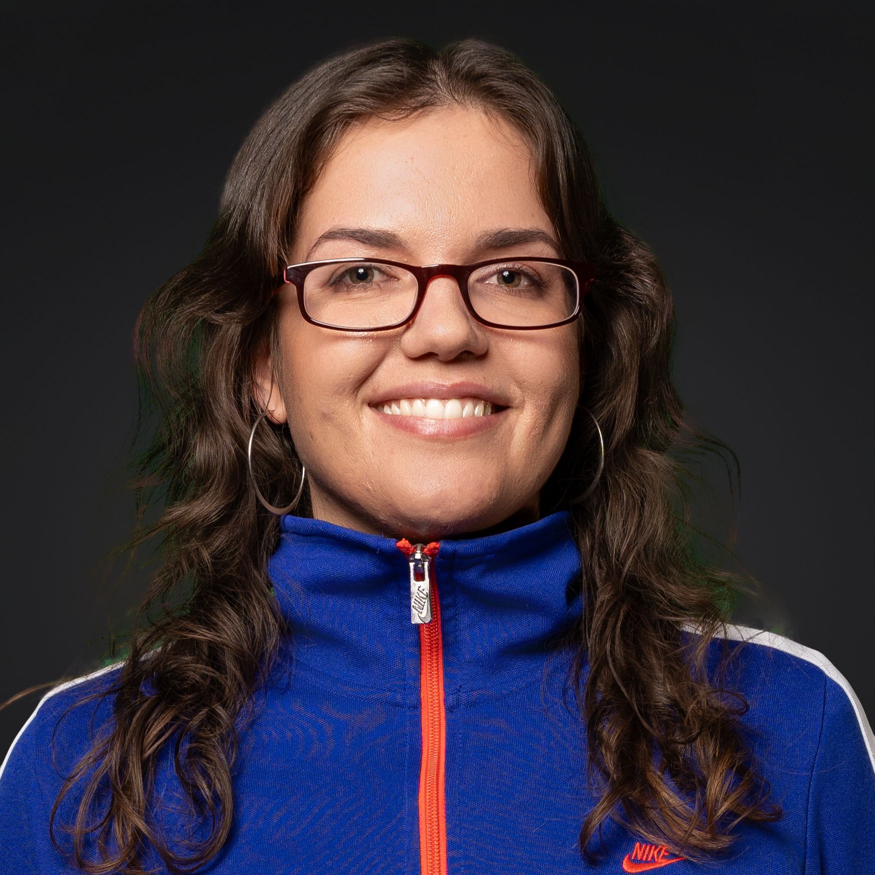 Frau mit Brille in blauer Nike-Jacke mit Reißverschluss und rotem Akzent.