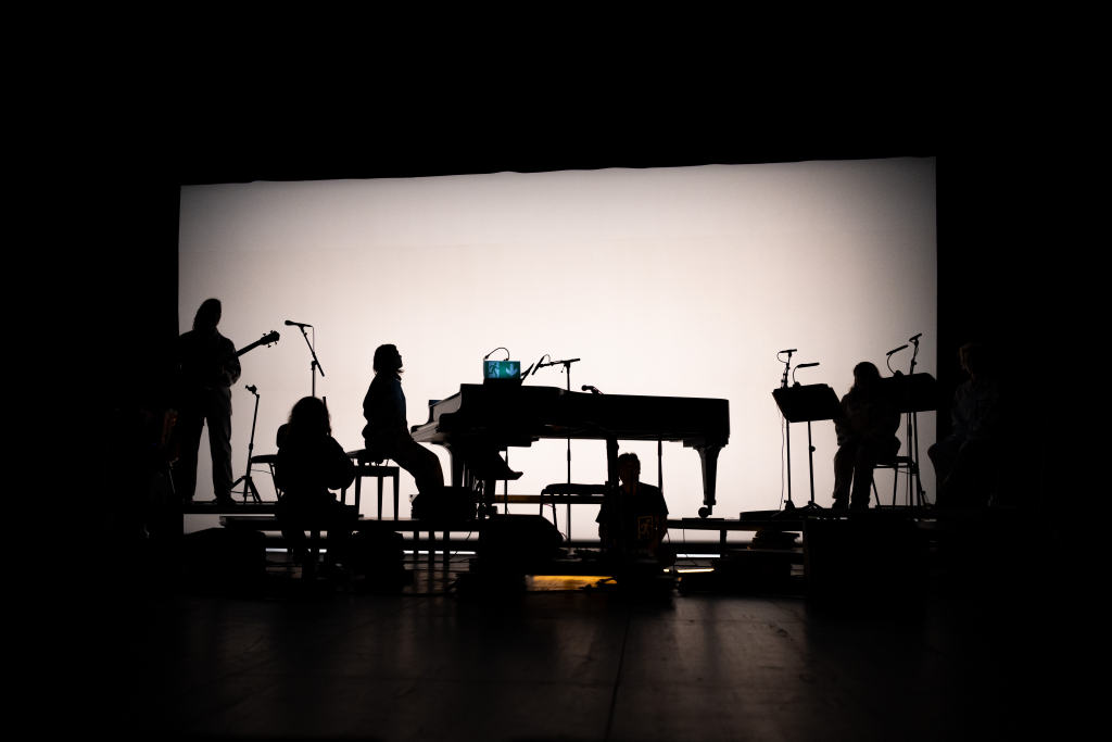 Silhouette einer Live-Band auf der Bühne mit einem Klavier und Mikrofonen im Hintergrund.