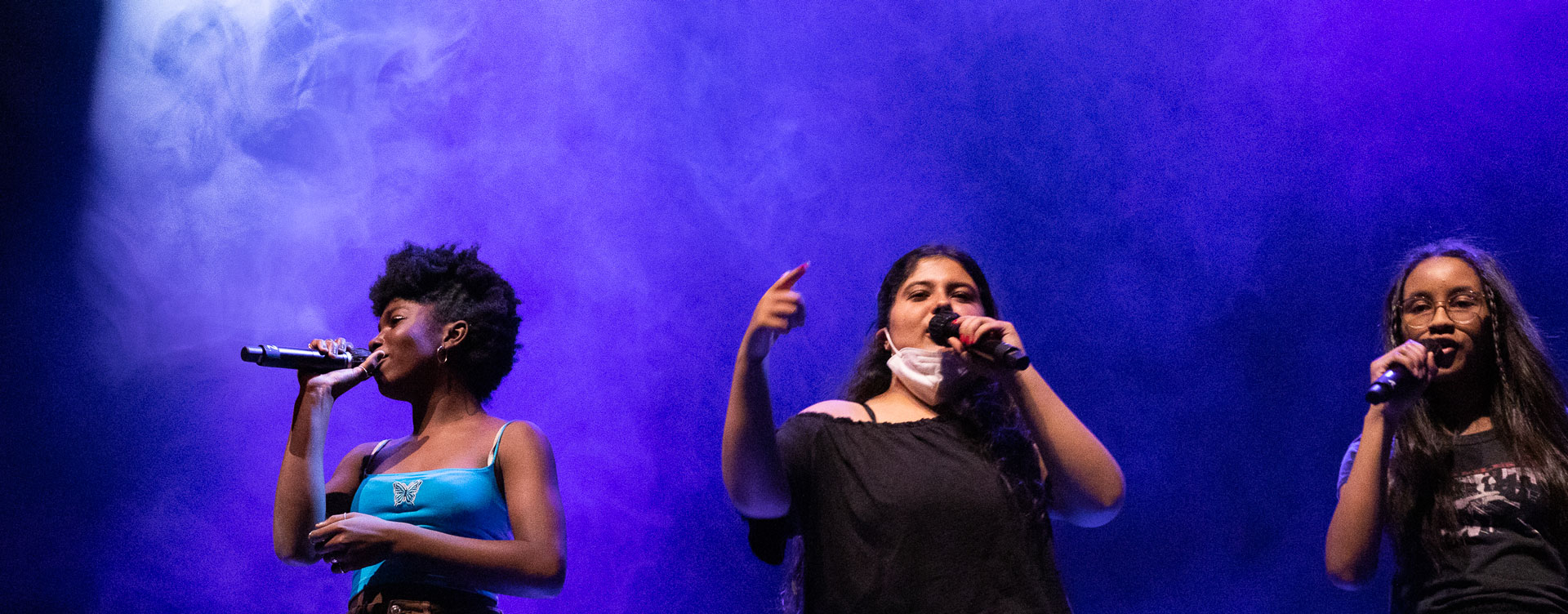 Drei Mädchen stehen auf der Bühne mit jeweils einem Mikrofon in der Hand und rappen.